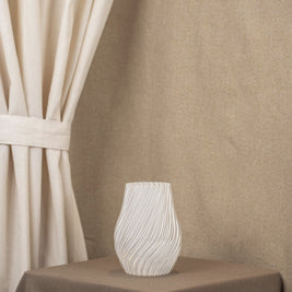 Vintervad Design Ida vase in clear, biodegradable material with elegant spiral patterns on a brown table.