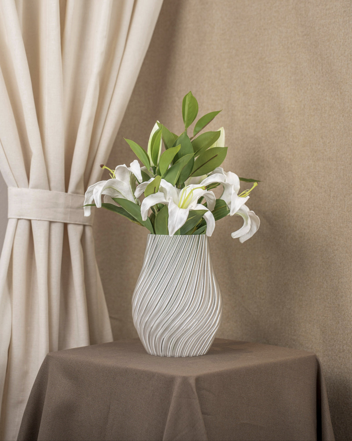 Vintervad Design Ida vase in clear, eco-friendly material with a wavy spiral pattern holding white lilies on a table.