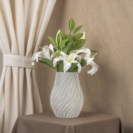 Vintervad Design Ida vase in clear, eco-friendly material with a wavy spiral pattern holding white lilies on a table.